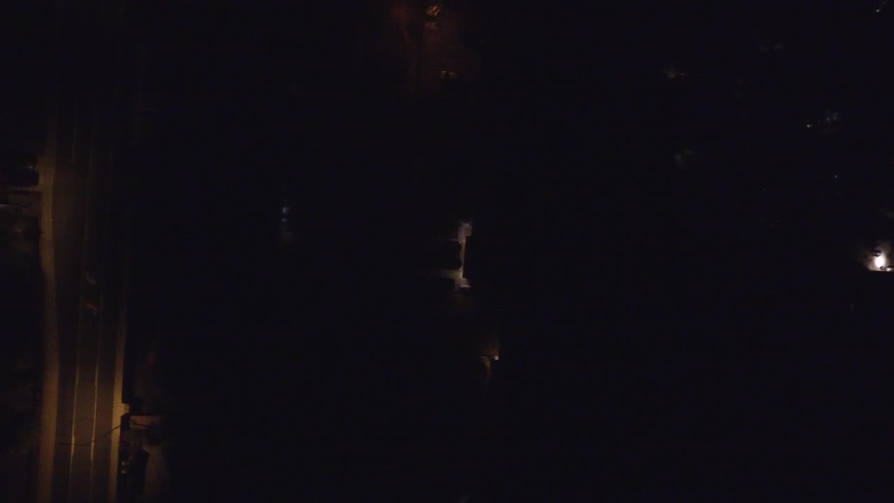 Dark neighborhood scene with a small streetlamp glow and faint tree silhouettes.