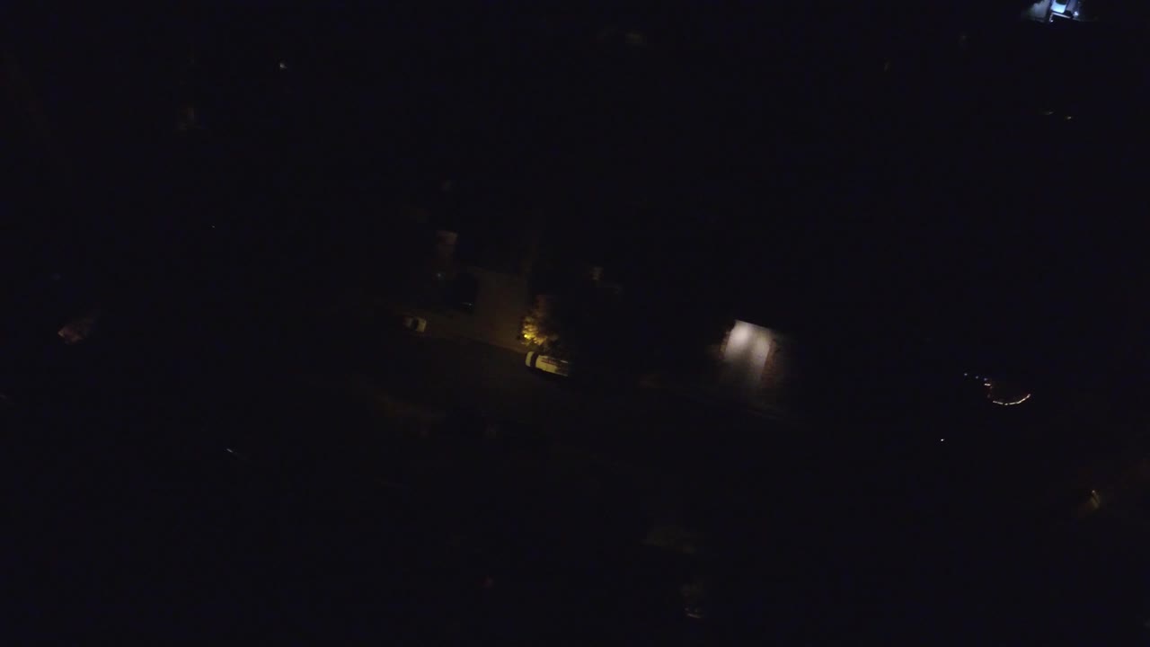 Early frame of the Hidden Lake night aerial, showing sparse warm building lights and faint dark land shapes with no visible people.