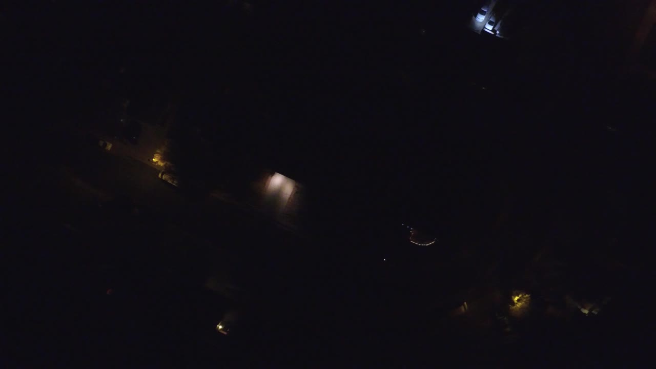 Dim aerial frame over Hidden Lake, Colorado showing warm road lights, a cool white building light near the top, faint roofs, and no visible people.