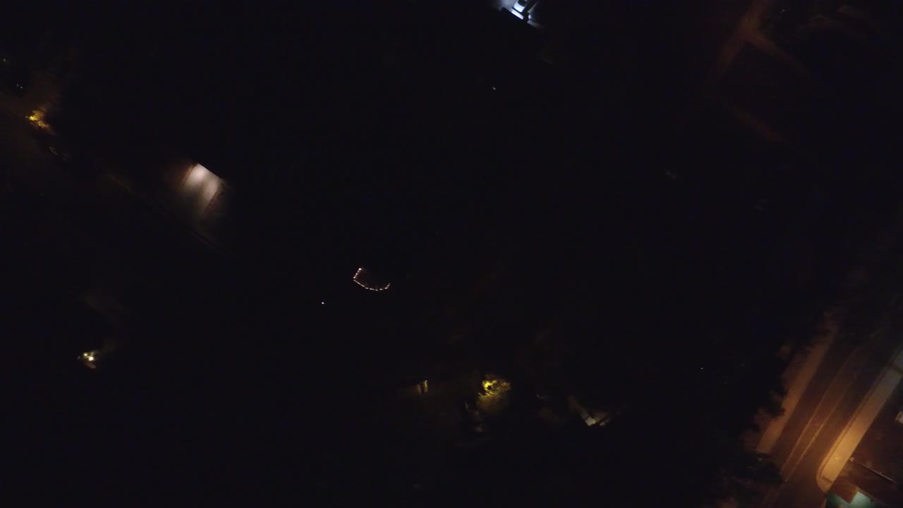 Overhead night frame in Hidden Lake, Colorado with an amber-lit road segment near the lower right, scattered small lights, heavy darkness, and no visible people.