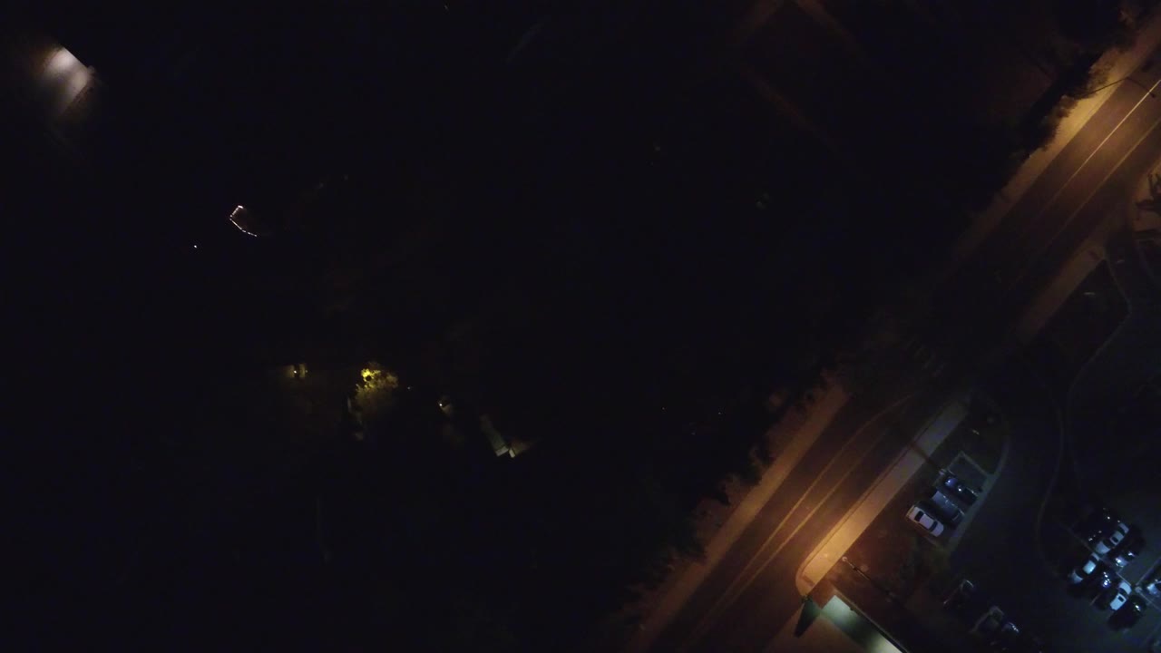 Overhead night view in Hidden Lake, Colorado showing a diagonal amber-lit road, a small parking area, shadowed trees or buildings, and no visible people.