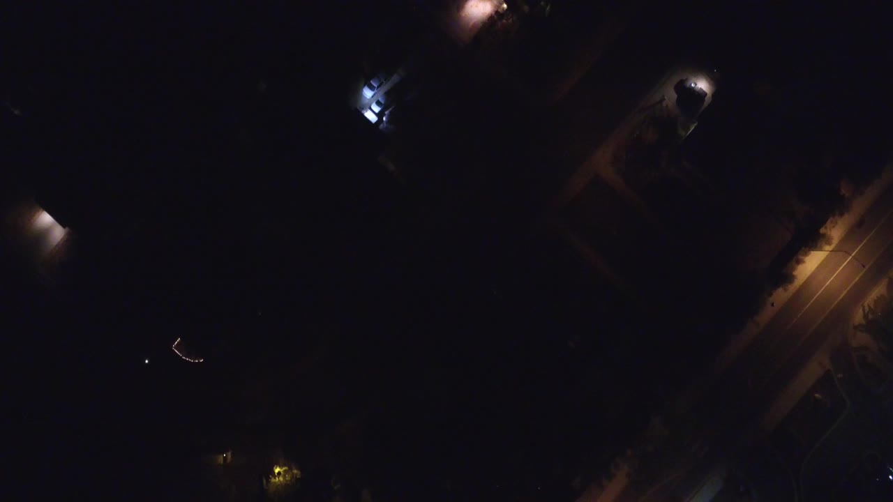 Dark aerial view of a lit road and scattered house lights at night.