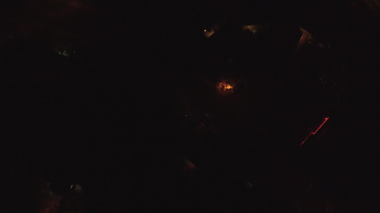 Dark overhead residential area with faint lights and a red diagonal trace.