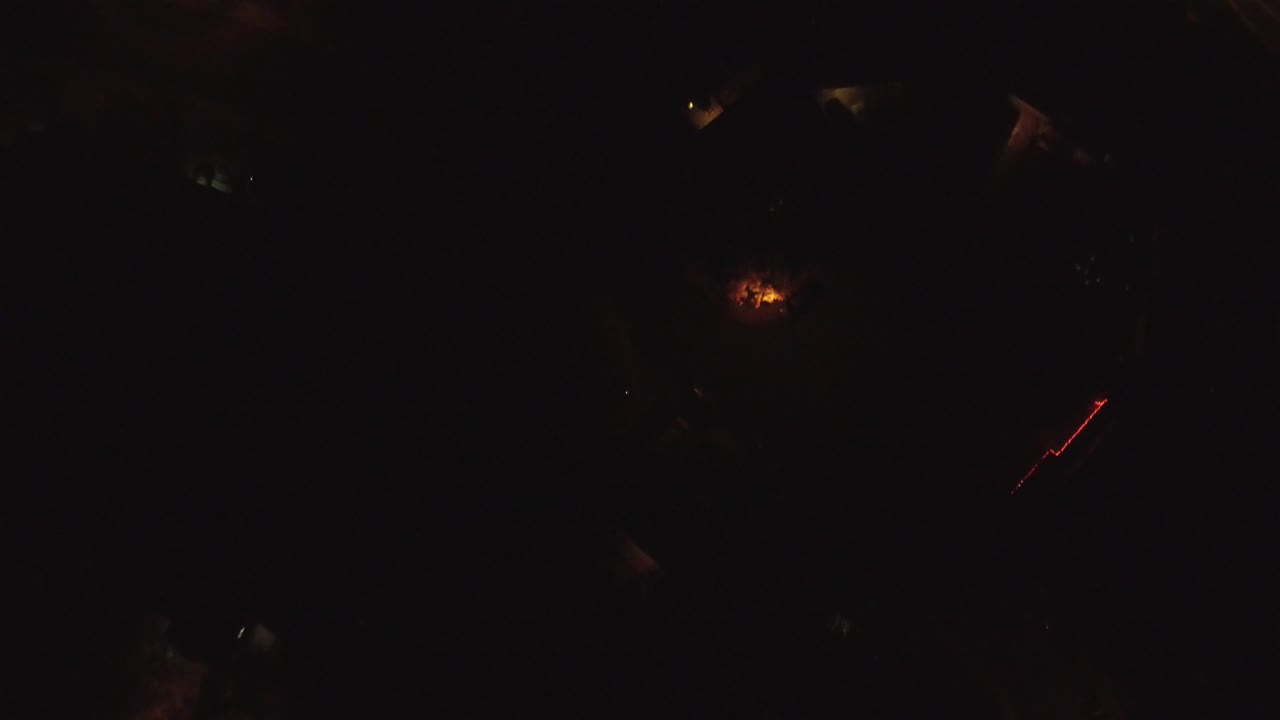 Second frame from the Hidden Lake, Colorado clip, with the red streak slightly right of center amid black terrain, dim roof shapes, and isolated warm lights, no visible people.