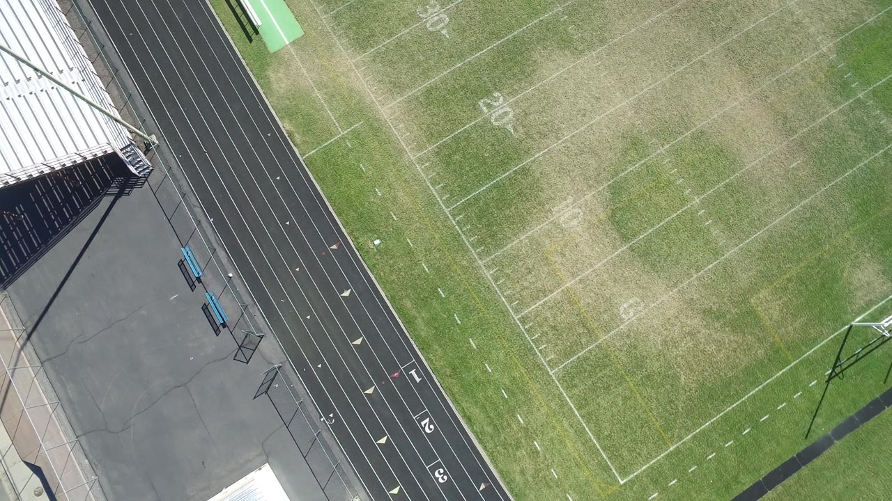 Top-down view in Hidden Lake, Colorado with metal bleachers at the upper edge, a black running track below, green benches near the field, and no visible people.