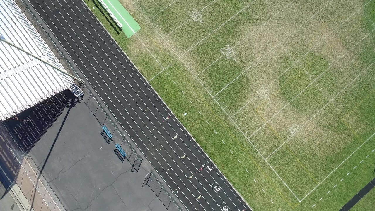 Overhead view of bleachers casting shade beside a running track and football field.