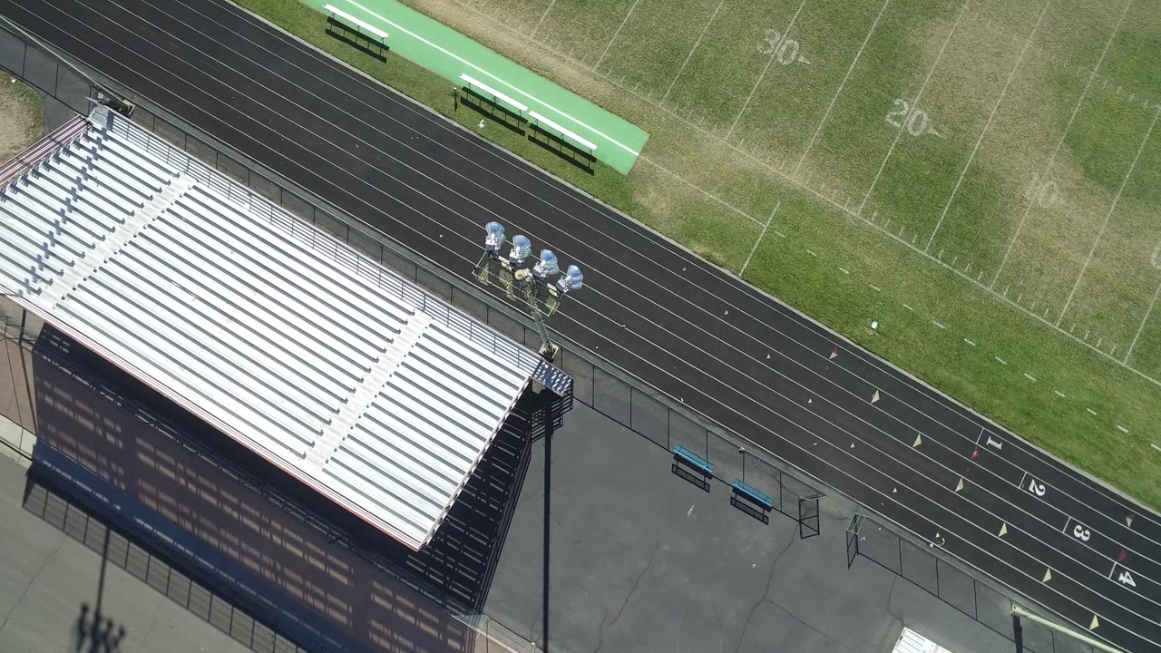 High oblique aerial view in Hidden Lake, Colorado with the white bleacher rows dominating the lower frame, black track lanes above, green field lines, and no visible people.