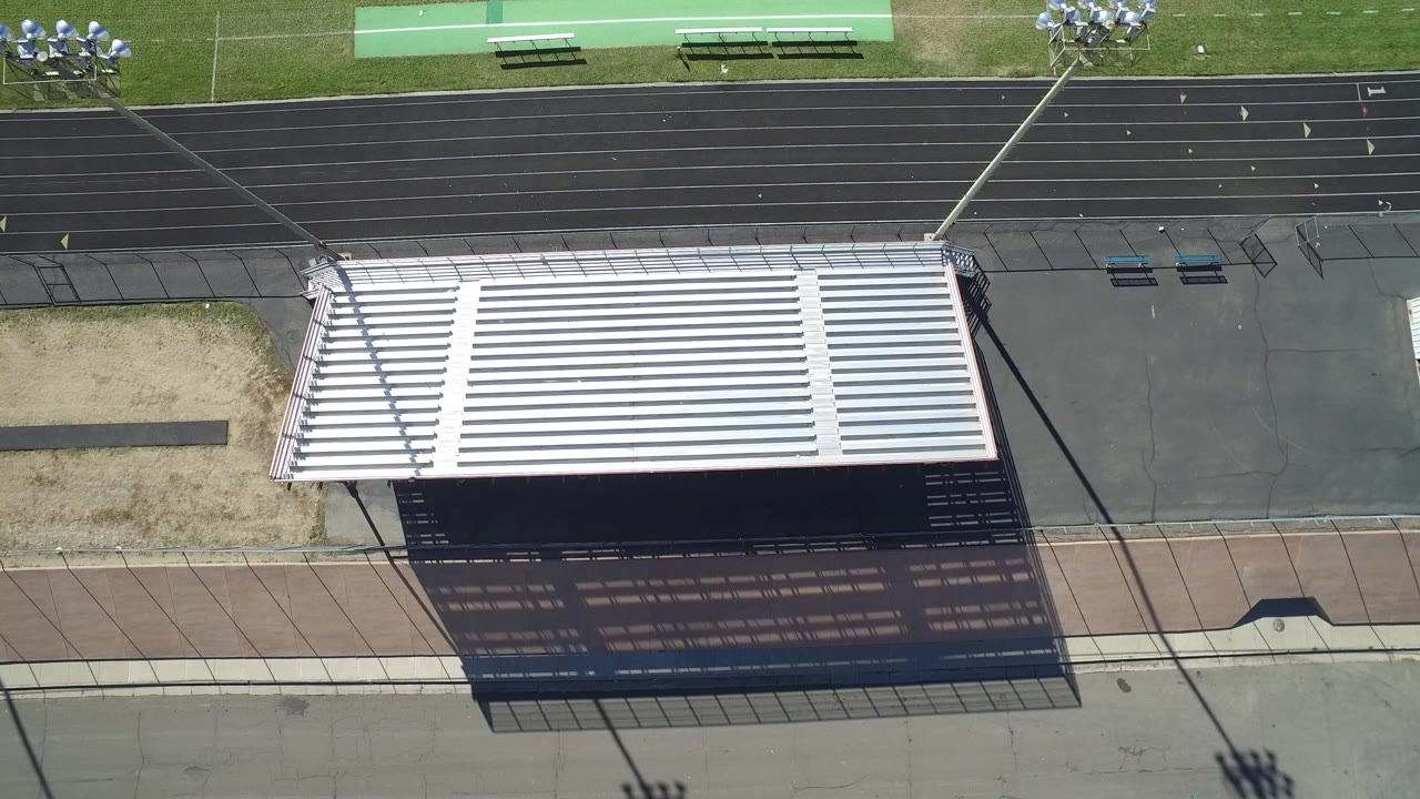 Overhead view of bleachers beside a black running track and football field.