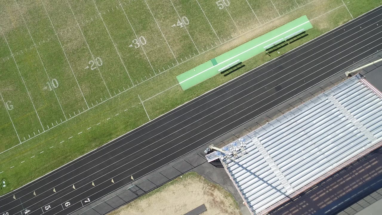 Overhead aerial frame of a Hidden Lake, Colorado football field with yard numbers, a black running track, silver bleachers, and no visible people.