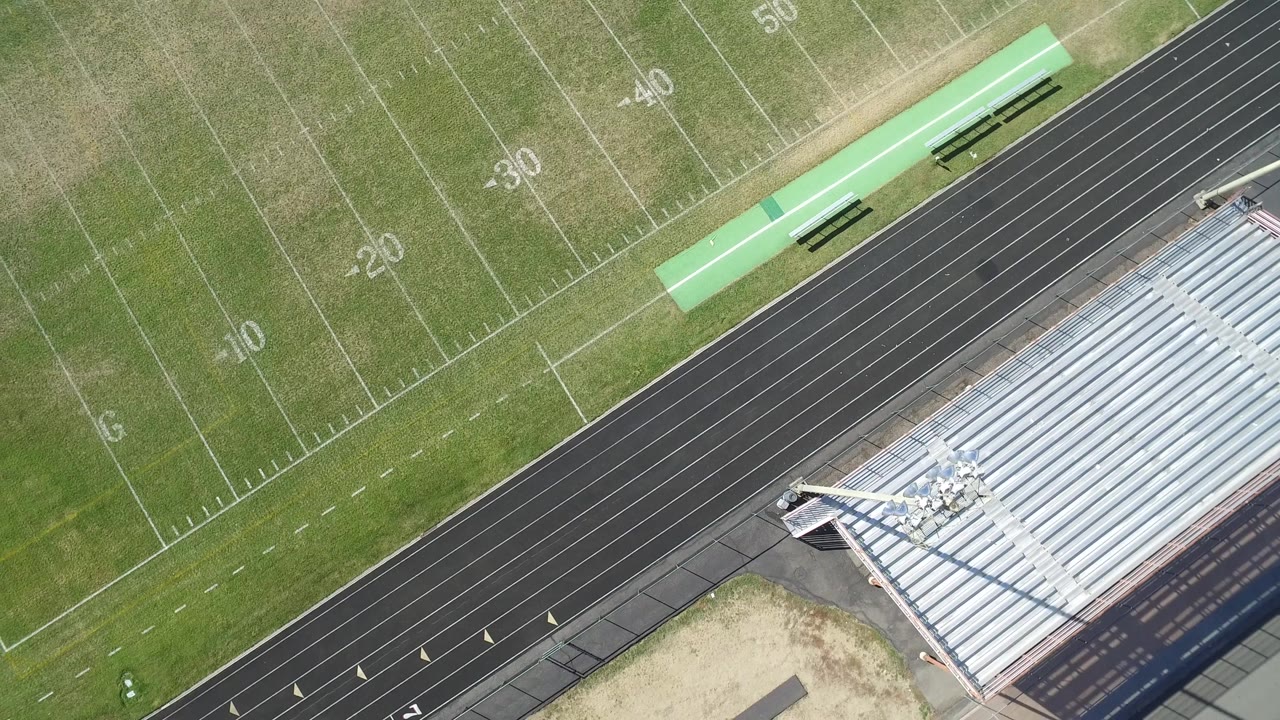 Drone view of a football field corner, running track, and stadium seating.