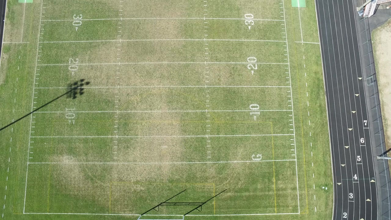 Overhead view of a marked grass football field beside a running track.