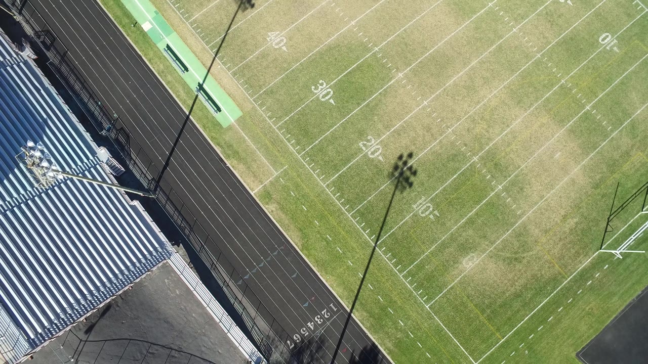 Aerial corner of football field with bleachers, track, and field goal post.