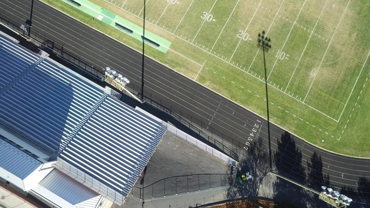 Overhead view of bleachers, running track, and football field markings.