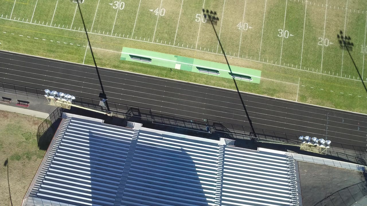Overhead view of bleachers, running track, and football field markings.