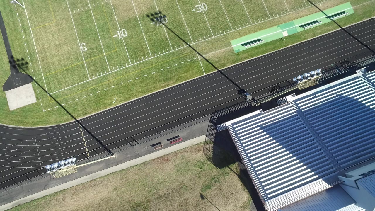 Overhead view of a football field, running track, and empty bleachers.