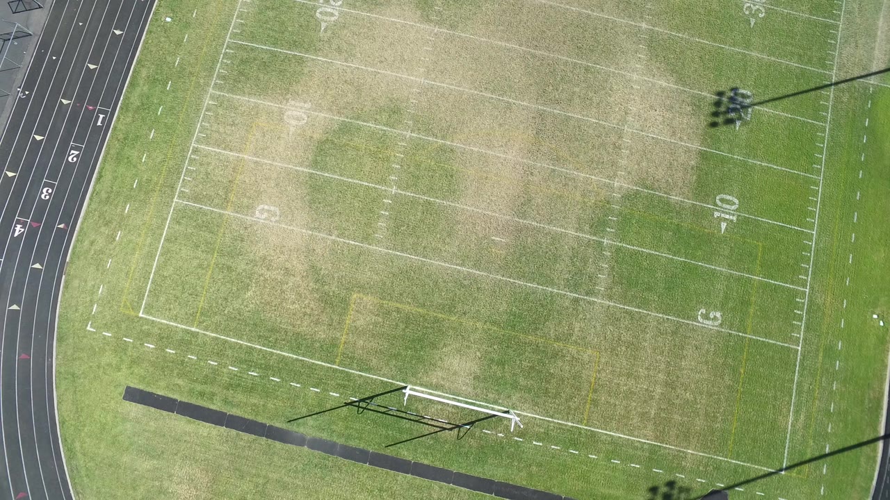 Top-down football field with goalpost and track at the frame edge.
