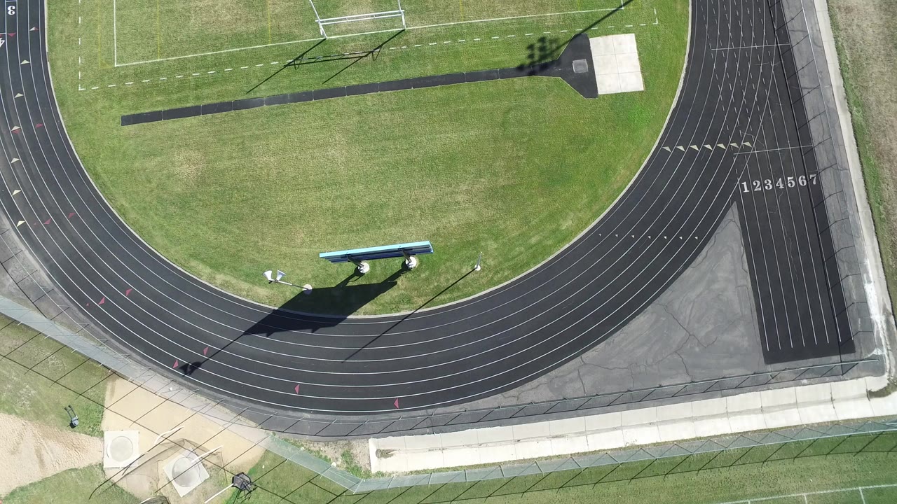 Top-down aerial view of a black running track beside green athletic fields.