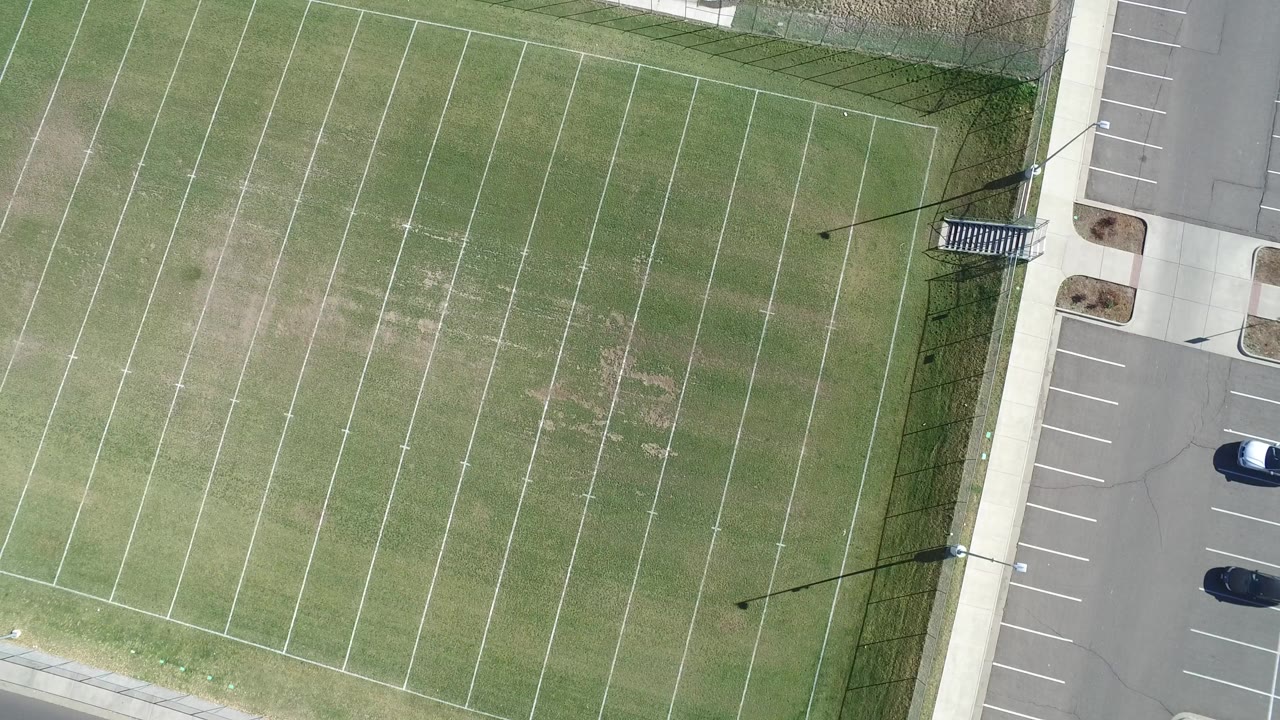 Top-down aerial frame in Hidden Lake, Colorado showing a green lined athletic field at left, a paved parking area at right, and no visible people.