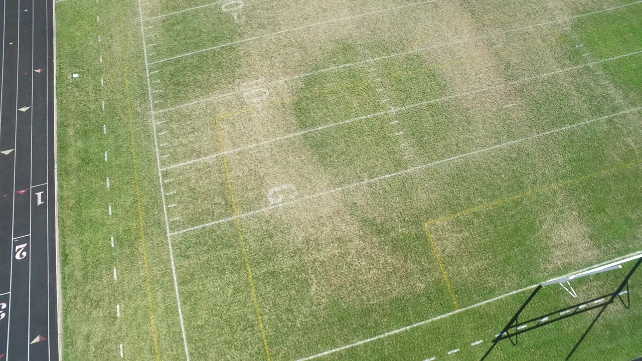 Overhead frame of a Hidden Lake, Colorado football field with white yard lines, faded grass patches, part of a black running track at the left edge, and no visible people.