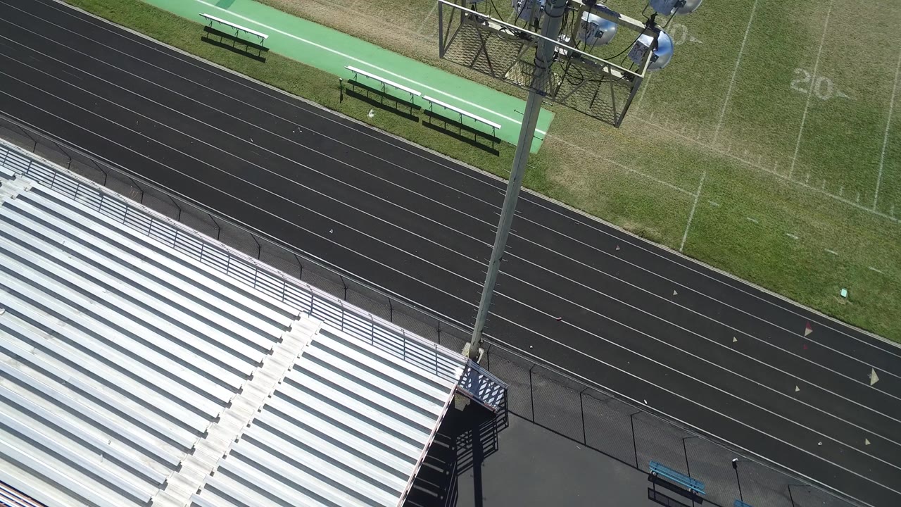 High aerial view of bleachers, track lanes, light pole, and field sideline
