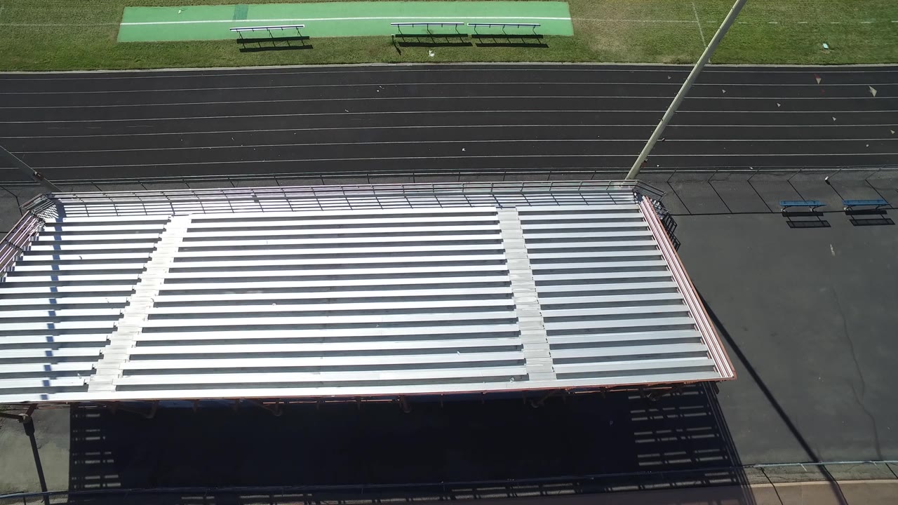 Aerial view in Hidden Lake, Colorado showing the bleacher roofline lower in frame, track lanes across the middle, sideline mats and benches above, and no visible people.