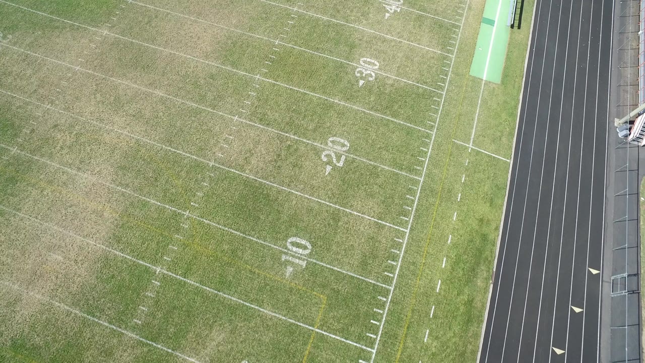 High overhead frame of a Hidden Lake, Colorado football field with white 10, 20, and 30 yard numbers and a dark running track along the right side, no visible people.
