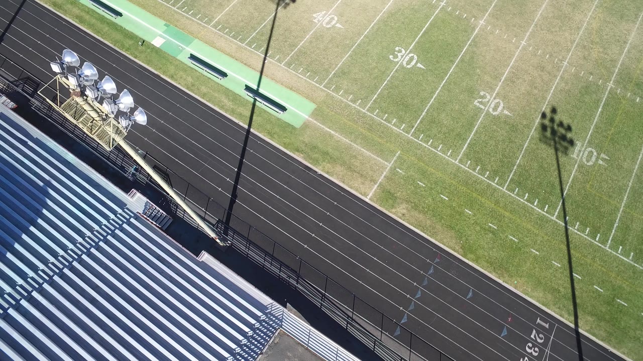 High angle over the track, field markings, and a light pole shadow.