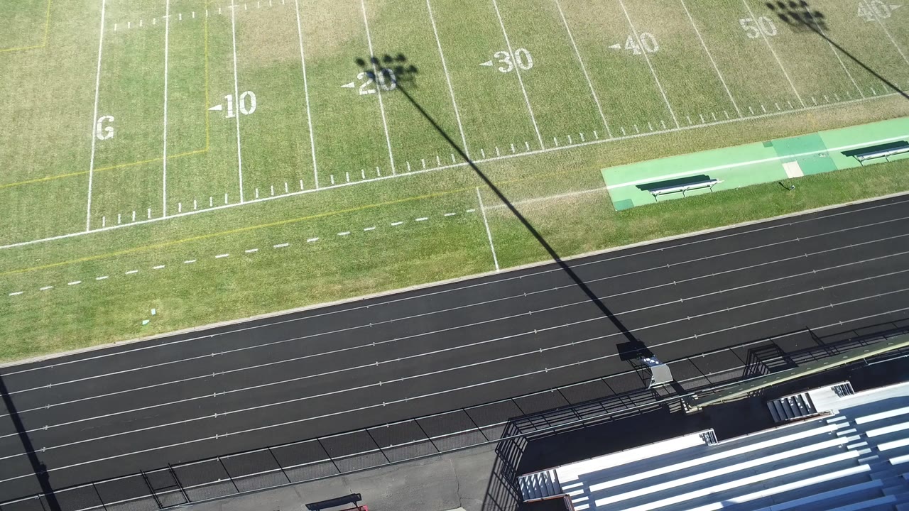 Overhead frame from Hidden Lake, Colorado showing white football yard lines, a black running track, bleachers at the lower right, and no visible people.