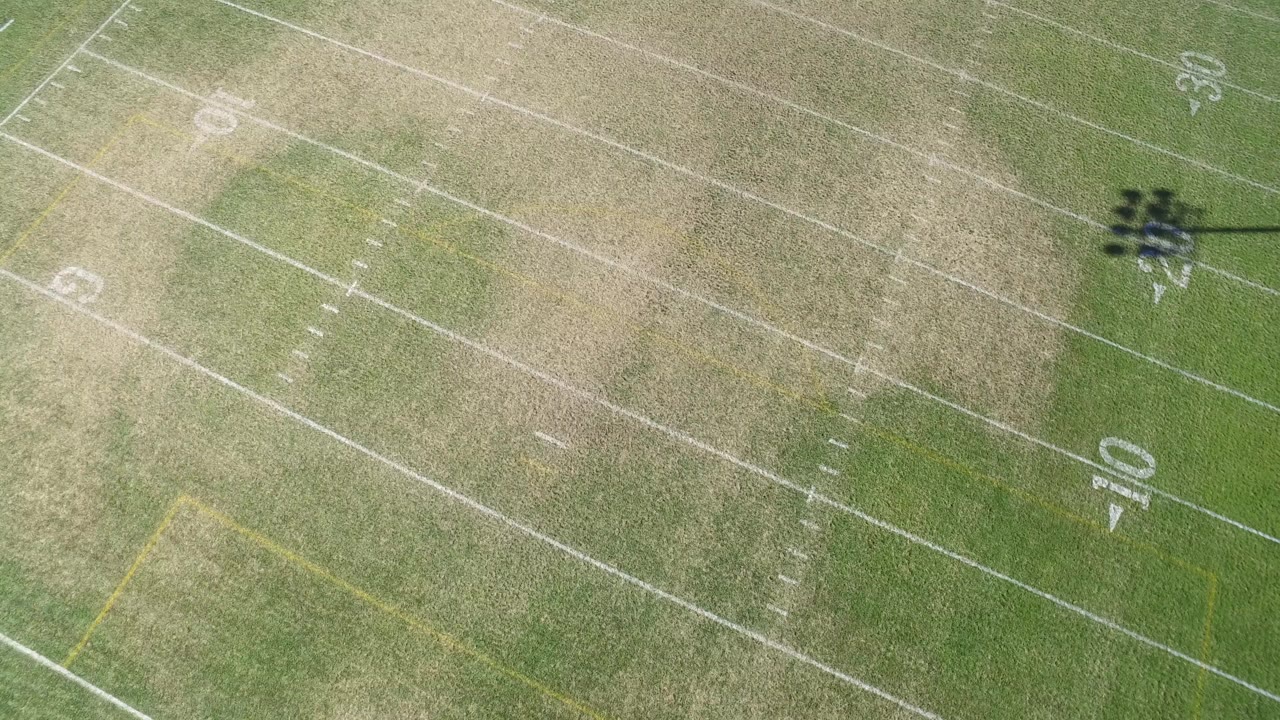 Overhead view of a Hidden Lake, Colorado football field with white yard lines, worn green and tan grass, and no visible people.