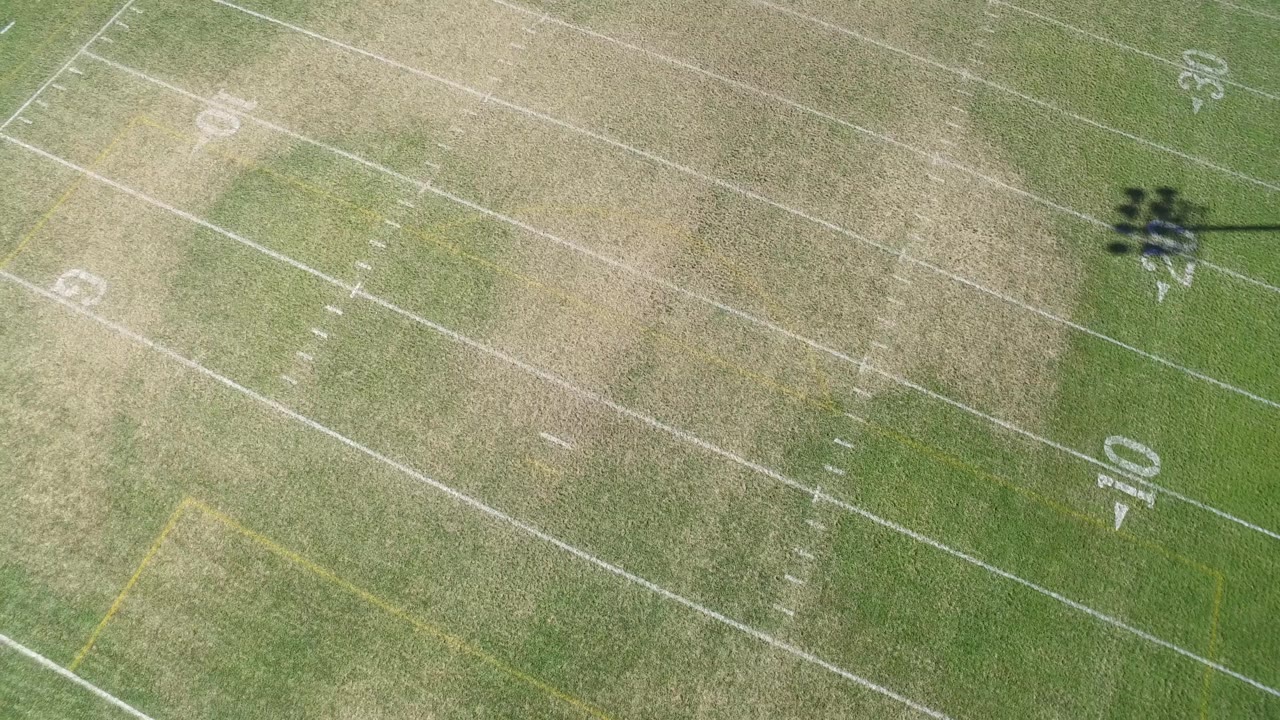 High overhead frame of the Hidden Lake football field showing worn turf, white yard numbers, diagonal field lines, and no visible people.
