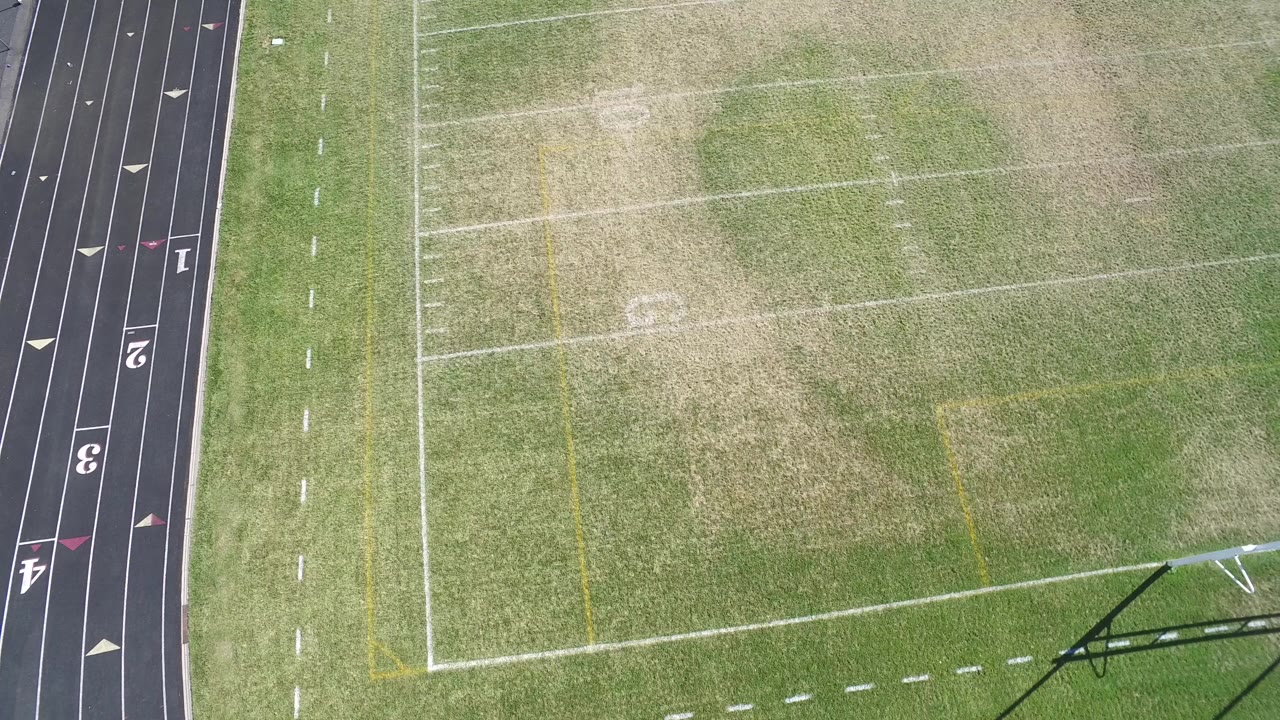 Top-down frame in Hidden Lake, Colorado, with the football field centered and black track lanes with numbers visible along the right edge, with no visible people.