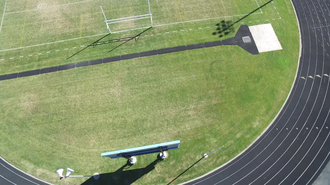 High aerial view in Hidden Lake, Colorado showing green athletic grass, a soccer goal, a curved black track, and a scoreboard structure near the lower edge, with no visible people.