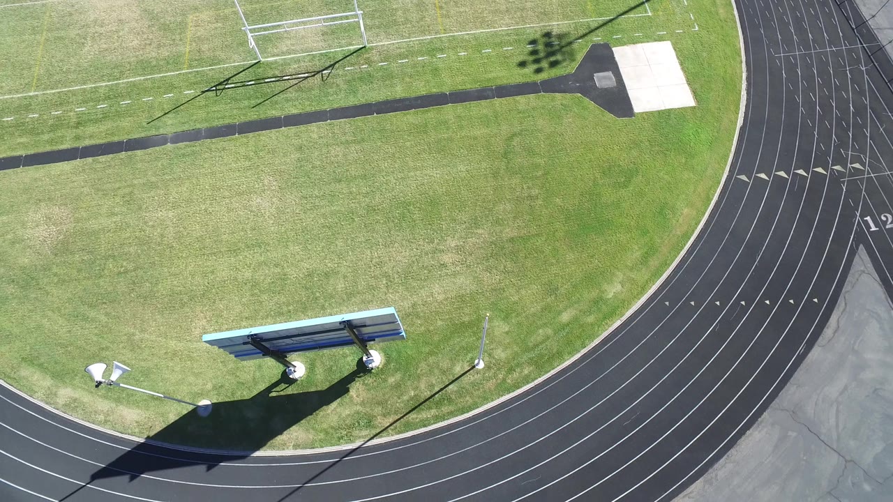Top-down view of track bend, field grass, scoreboard, and lane numbers.