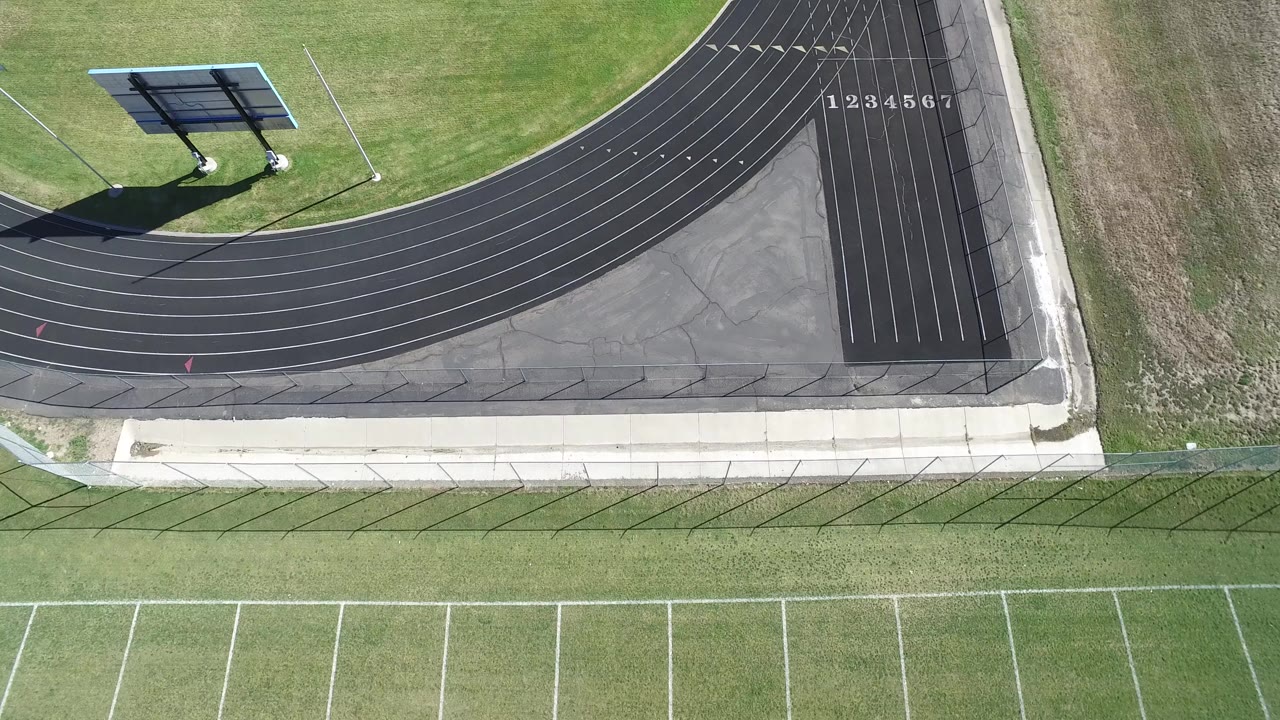 Overhead frame in Hidden Lake, Colorado showing the curved black track, white field markings, grass, a paved path, and no visible people.