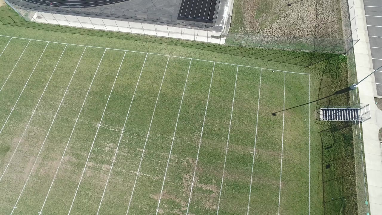Overhead football field with worn grass and sideline walkway.