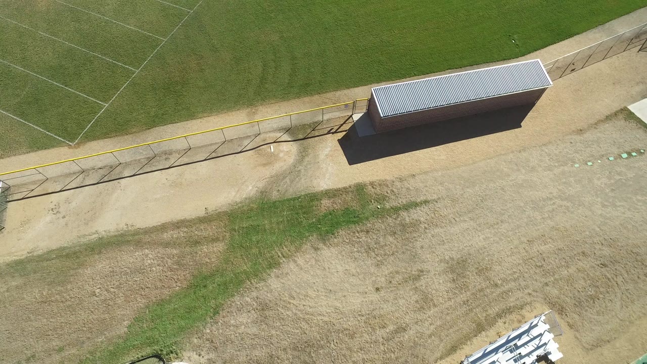 A high aerial moment in Hidden Lake, Colorado frames the small field building higher in view, with the fence crossing the dirt perimeter and no visible people.