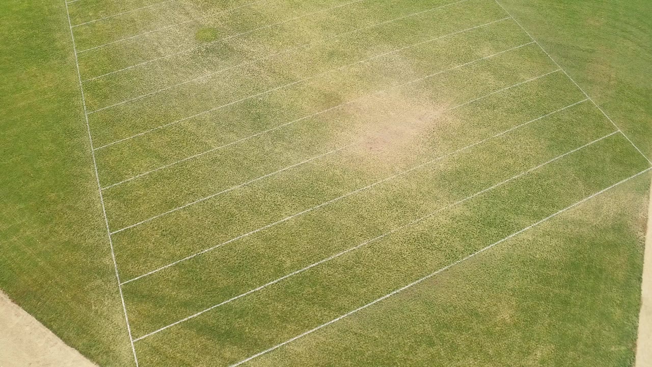 Overhead frame from Hidden Lake, Colorado showing a green field with diagonal white markings, light tan worn grass patches, and no visible people.