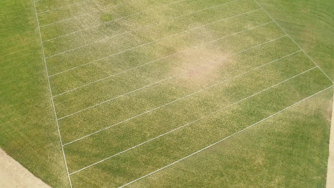 Overhead Hidden Lake, Colorado field frame with white diagonal lines crossing patchy green turf and a tan border visible at the lower right, with no visible people.
