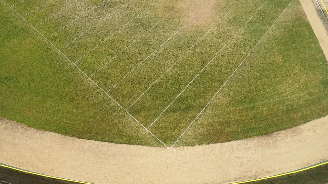 Aerial frame from Hidden Lake, Colorado with angled white lines crossing green grass and a pale dirt border along the lower edge, with no visible people.
