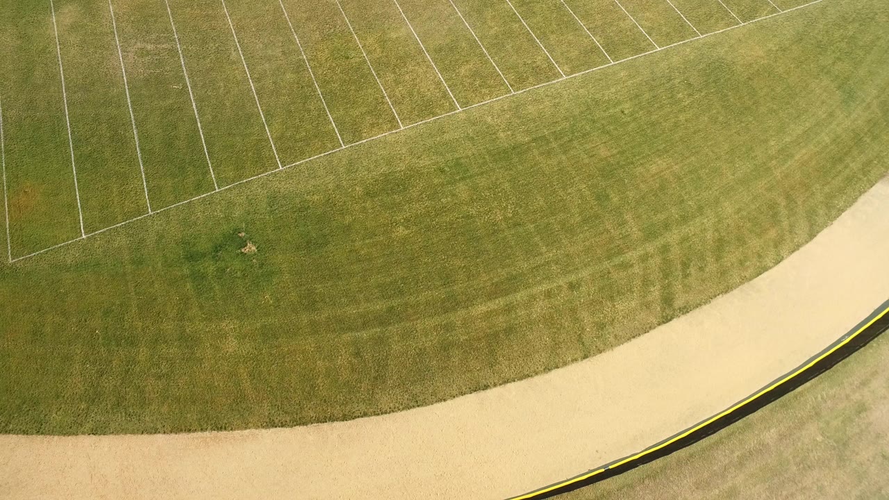 Top-down aerial frame in Hidden Lake, Colorado showing mowed green grass, faint white boundary lines, a pale curved path along the lower edge, and no visible people.