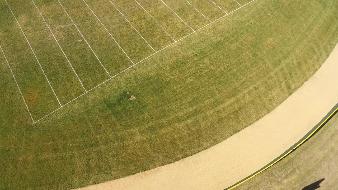 Top-down aerial frame near Hidden Lake, Colorado showing green grass, diagonal white field markings, and a pale curved road along the lower edge, with no visible people.