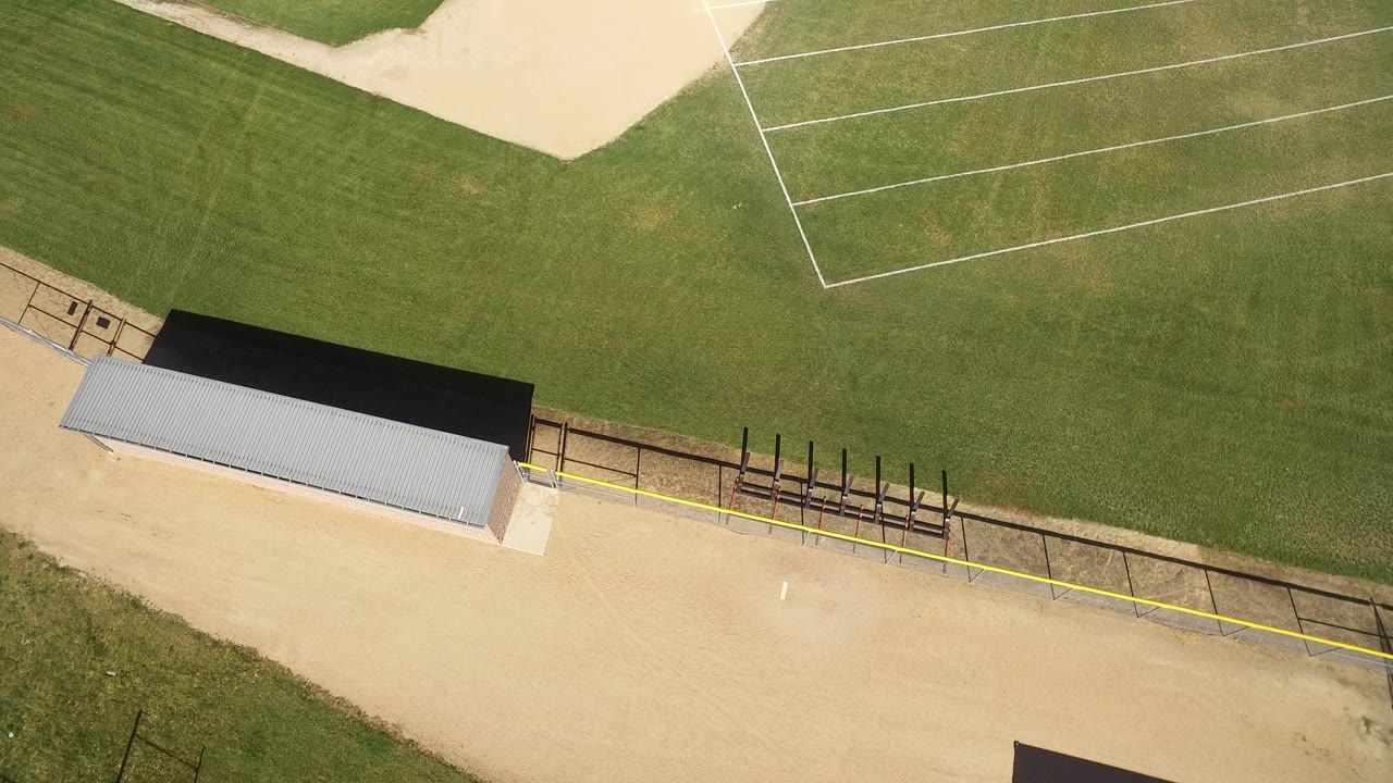 Overhead view of a baseball field edge with dugout roof and fencing.