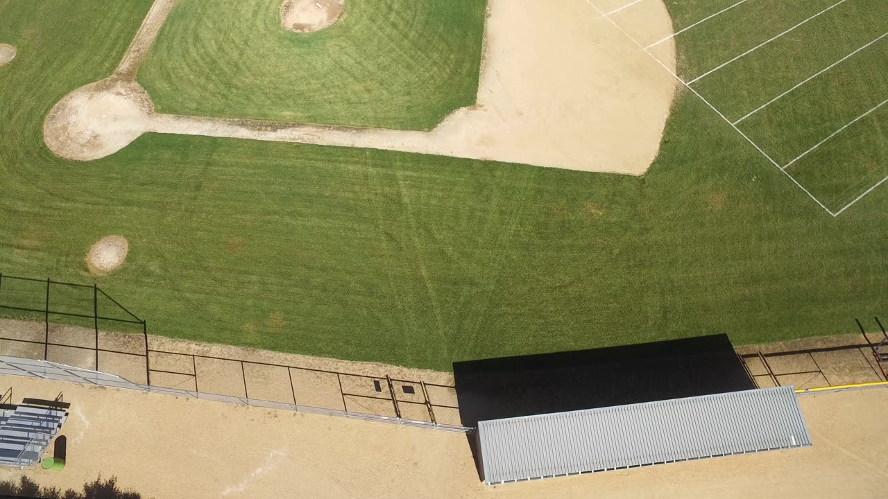 High overhead frame of a baseball field in Hidden Lake, Colorado, with green grass, tan infield dirt, bleachers, roofed structures, fencing, and no visible people.