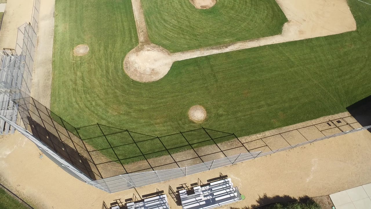 Second overhead frame of the Hidden Lake, Colorado field, with the infield fencing and lower-edge bleachers more centered against the green grass, no visible people.