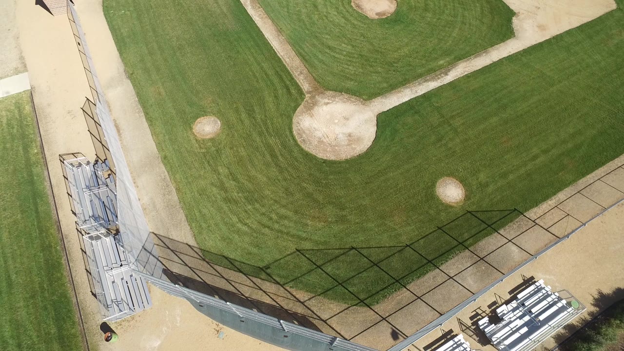 Overhead drone frame of a Hidden Lake, Colorado baseball field, showing mowed green grass, tan dirt areas, fencing, metal bleachers, and no visible people.