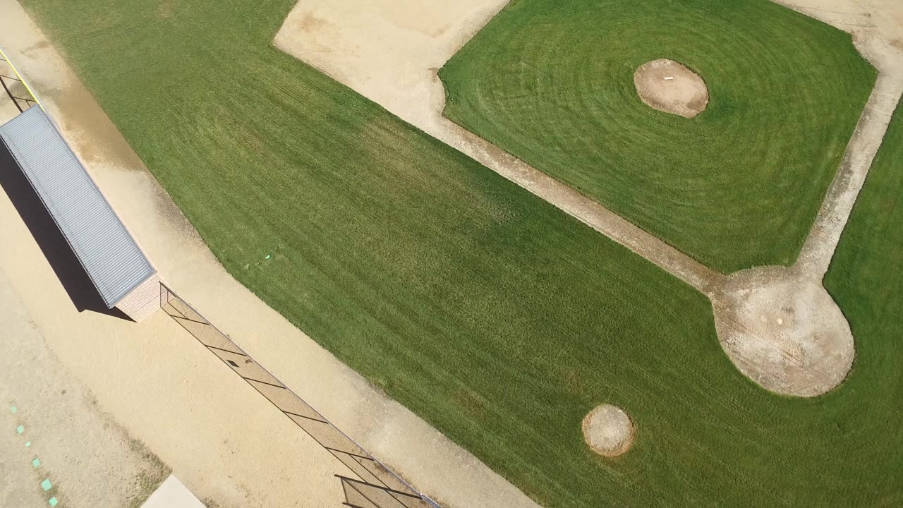 Top-down view of the Hidden Lake, Colorado baseball field, with the dirt infield and grass diamond high in frame, the shelter roof closer to center left, visible fence lines, and no visible people.