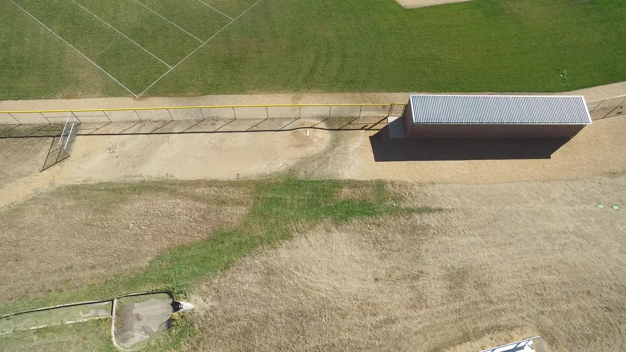 Overhead view of a marked green and tan sports field beside a fence and small roofed structure.