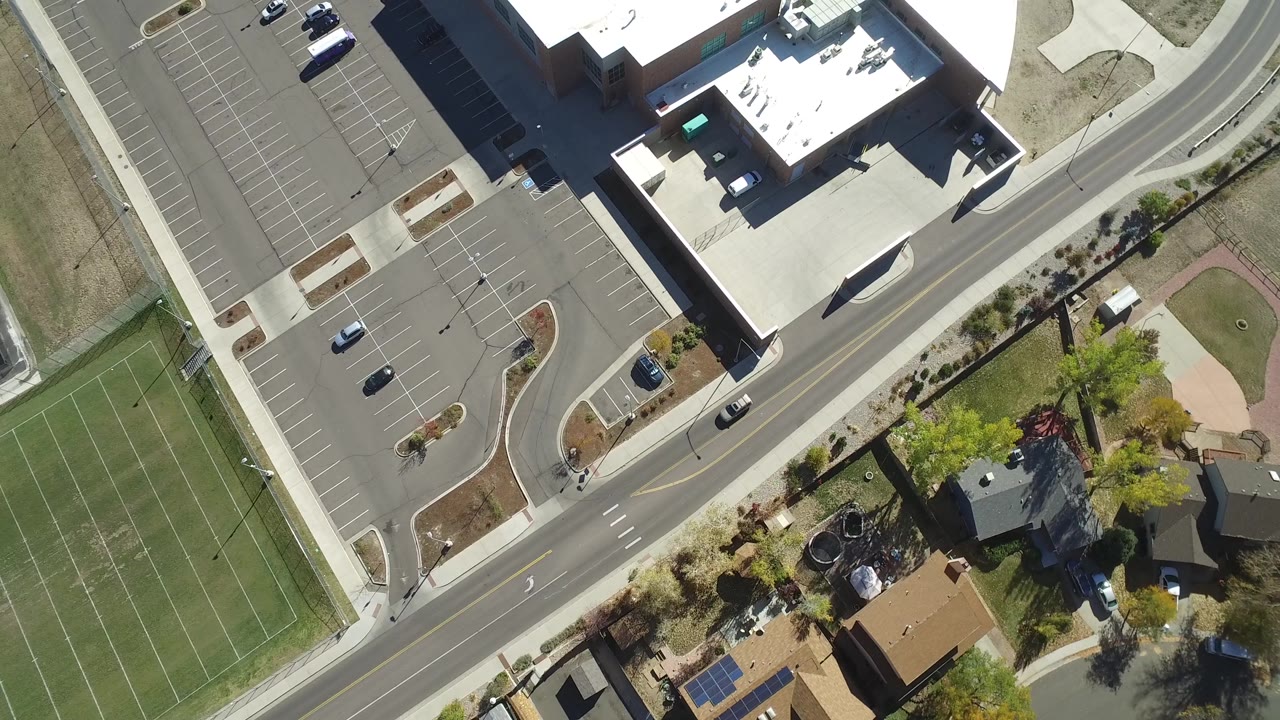 Overhead view of a building, curved road, parking lot, and ballfield area.