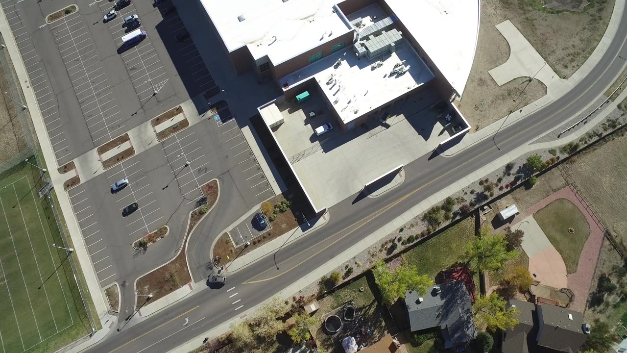 Second overhead frame in Hidden Lake, Colorado with the parking lot and a few cars on the left, the building roof near the top, the road through the center, and no visible people.