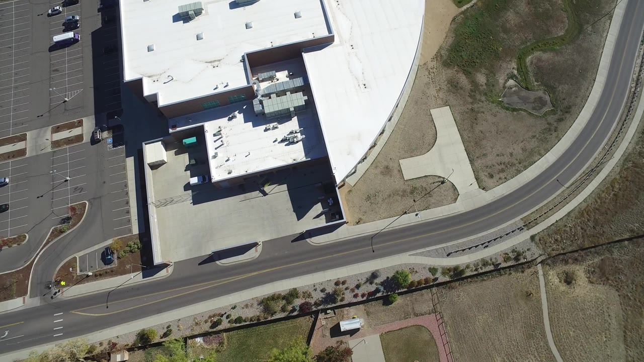 Overhead view of a white-roofed building beside a curved road and parking lot.